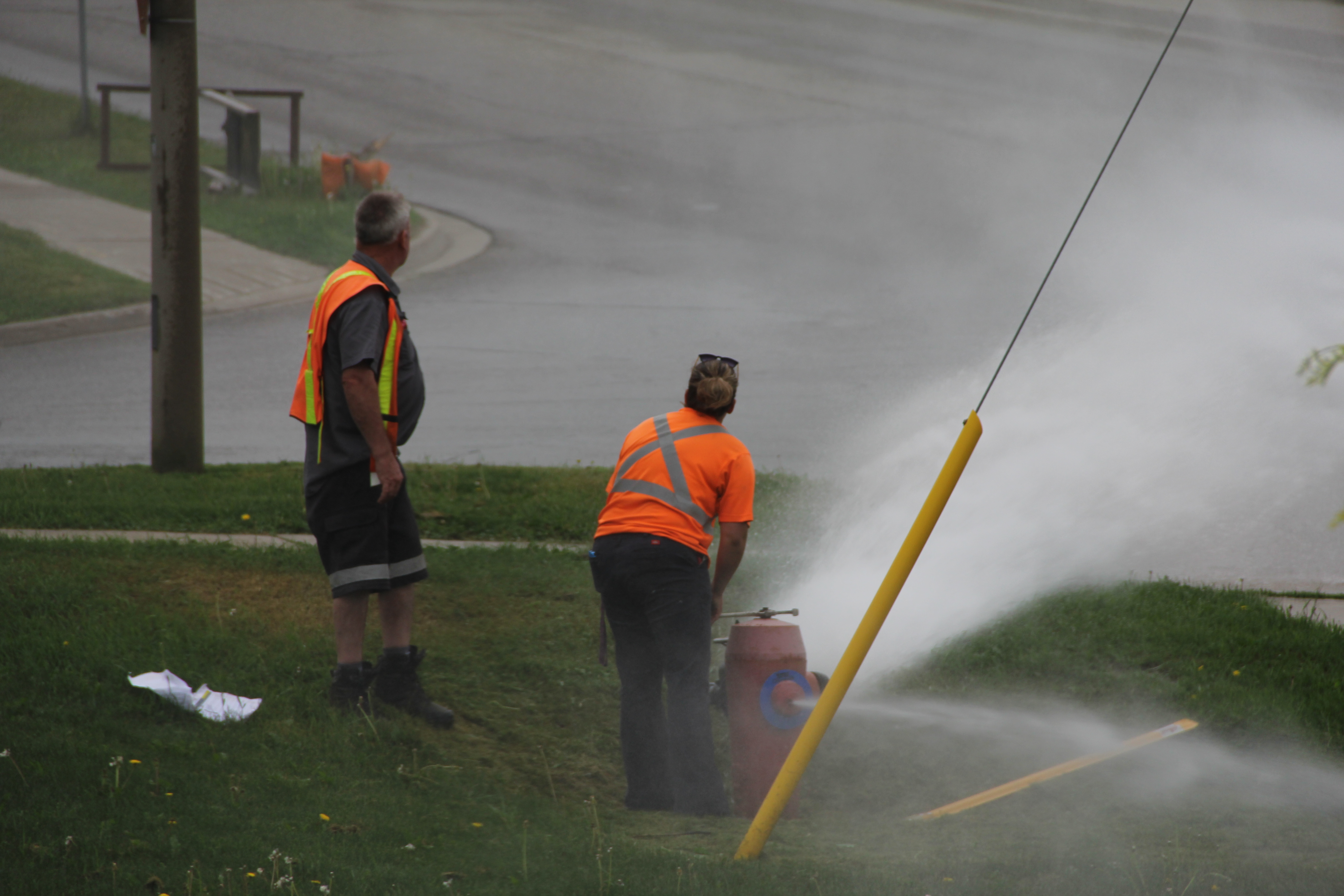 Two Waterworks Operators flushing a red fire hydrant on a street corner.